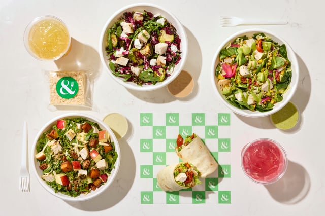 Overhead view of three salad bowls, a halved wrap, two iced drinks and a treat on marble