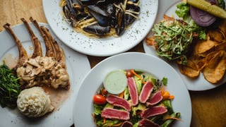 Overhead view of lamb chops, mussels linguine, seared tuna salad and a burger with chips