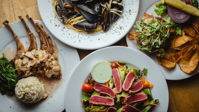 Overhead view of lamb chops, mussels linguine, seared tuna salad and a burger with chips