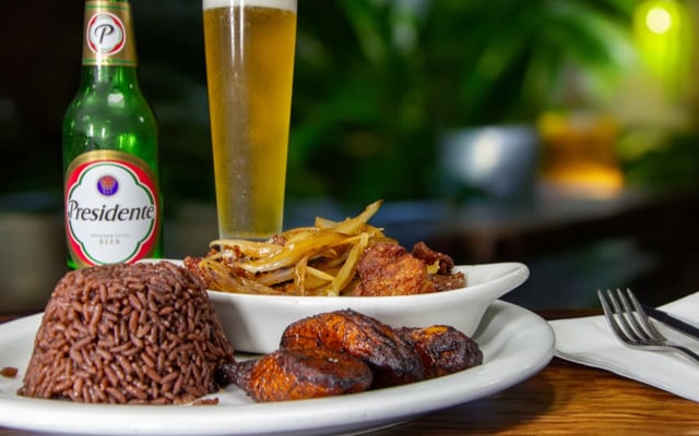 Plate of black beans and rice, sweet plantains and fried pork with onions beside a cold Presidente beer