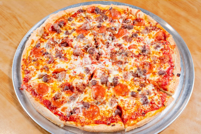 Whole pepperoni and sausage pizza with melted cheese on a metal pan atop a wooden table