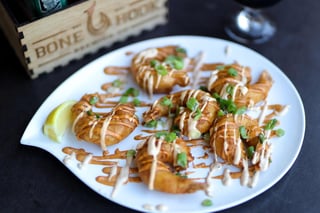 White plate of crispy fried shrimp drizzled with spicy sauce, scallions and a lemon wedge