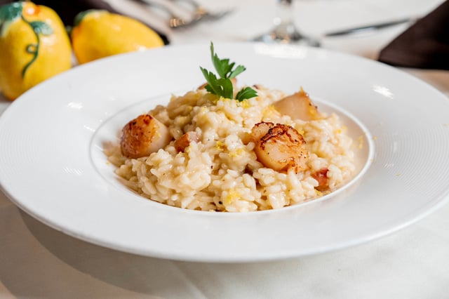 Seared scallops on creamy lemon risotto in a white bowl with ceramic lemons behind