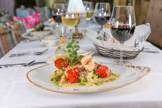 Plated lobster tail, shrimp and fish in light sauce on a set table with wine glasses