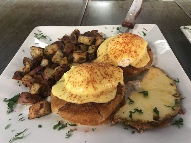 Two eggs Benedict on crispy crab cakes with hollandaise, paprika, herb-flecked home fries and pineapple