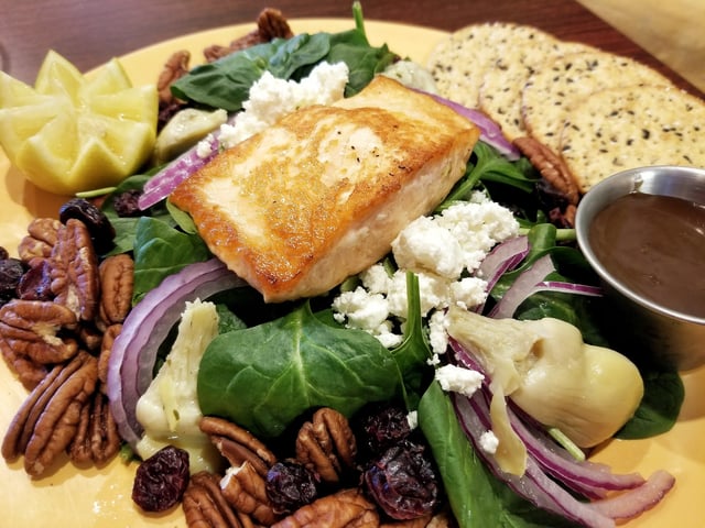 Seared salmon over spinach salad with pecans, feta, red onion, artichoke and crackers on a yellow plate