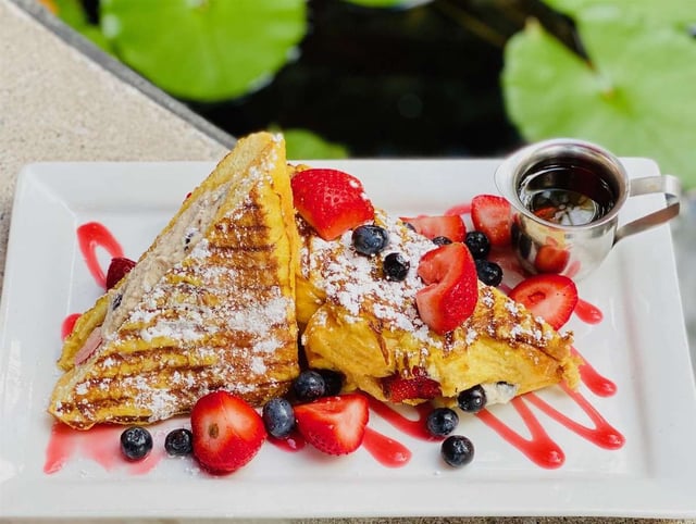 Grilled stuffed French toast dusted with powdered sugar, fresh strawberries and blueberries, with syrup, beside lily pads