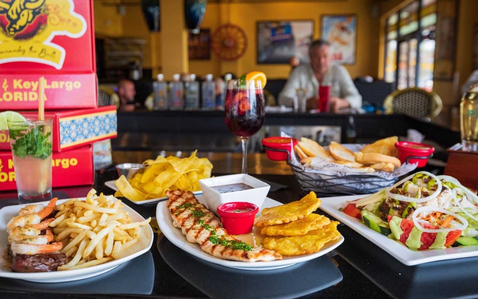Grilled chicken with tostones, shrimp and steak with fries, salad, sangria and mojito on a table in a yellow dining room