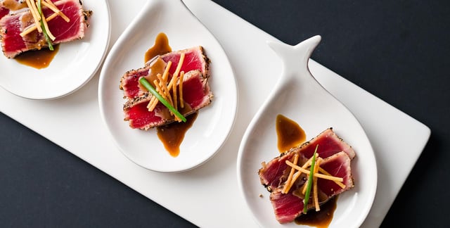 Three white teardrop dishes of peppered seared tuna with crispy potato strings and soy glaze
