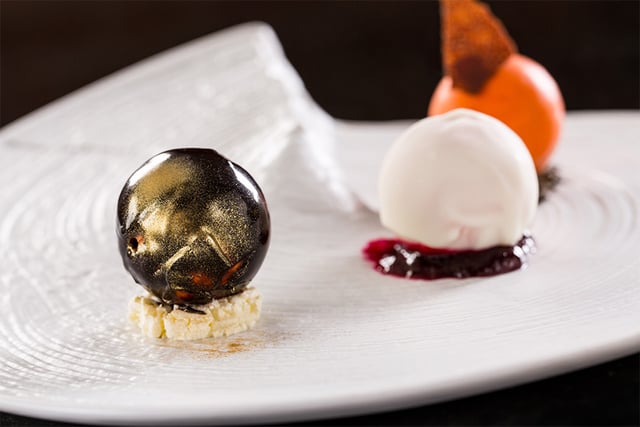 Elegant dessert plate with a gold-dusted dark chocolate sphere, white sorbet scoop and berry sauce