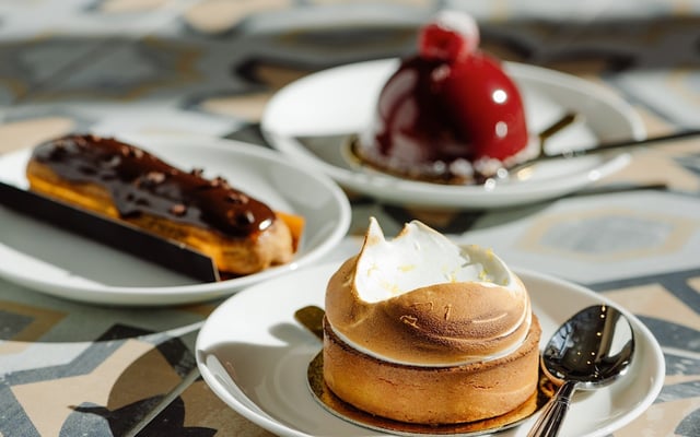 Toasted lemon meringue tart on a white plate with chocolate eclair and glazed raspberry dessert behind
