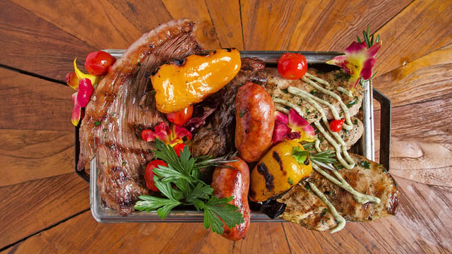 Overhead mixed grill platter of steak, chorizo, chicken and roasted peppers garnished with edible flowers