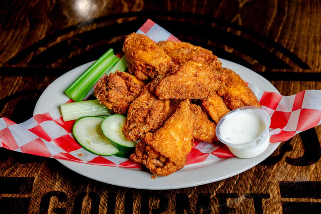 Crispy golden fried chicken wings on checkered paper with celery, cucumber slices and ranch dip