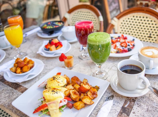 Outdoor breakfast table with lobster eggs Benedict, fresh juices, coffee and fruit on a cafe patio