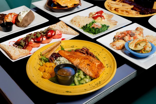 Table of plated dishes including seared salmon salad on a yellow plate, caprese, fish and steak with lobster tail