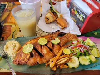 Whole fried red snapper with lime slices, rice, fries and fresh salad on a glass platter