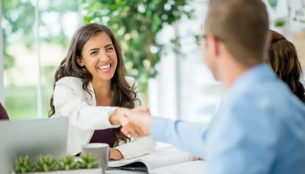 A new real estate agent joyfully shaking hands with clients, celebrating a successful deal.