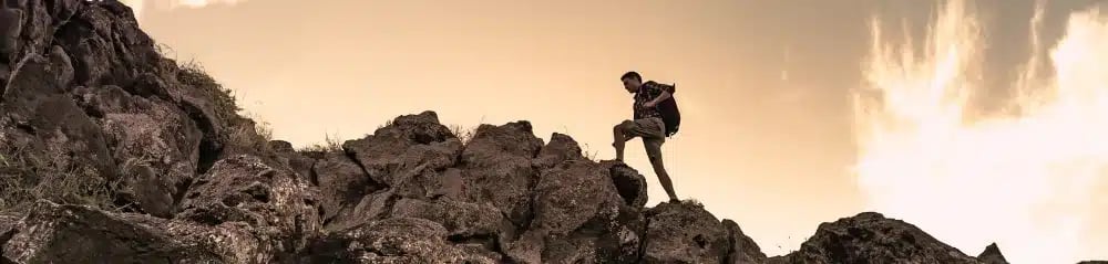 Person climbing a rocky hill, representing the challenge of setting realistic goals in real estate