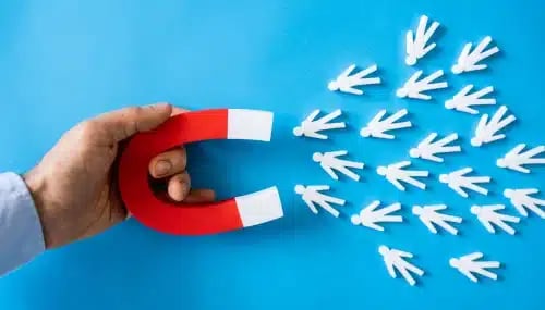 Hand holding a magnet attracting paper cutouts of people, representing lead generation in real estate and the importance of