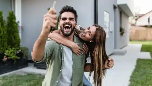 A happy couple celebrating outside their new home with keys, assisted by a buyer agent.