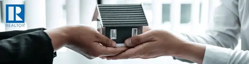 Hands holding a miniature house with the REALTOR® logo, illustrating a buyer agent explaining new NAR rules
