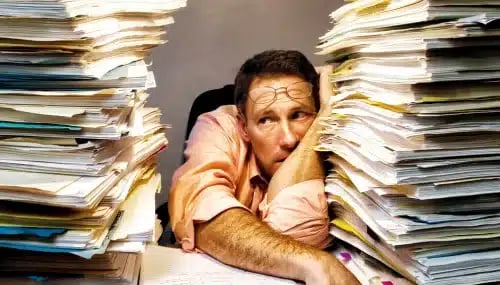 real estate buyer agent problems displayed by a man leaning on a stack of paperwork.