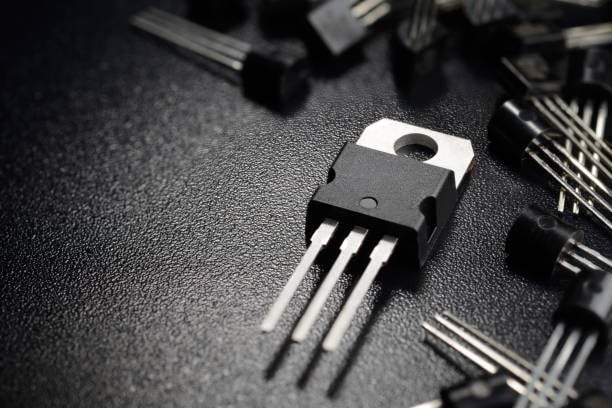 imagem de transistores de potência em um circuito eletrônico sobre uma superfície escura, destaque para componente com três pinos metálicos.