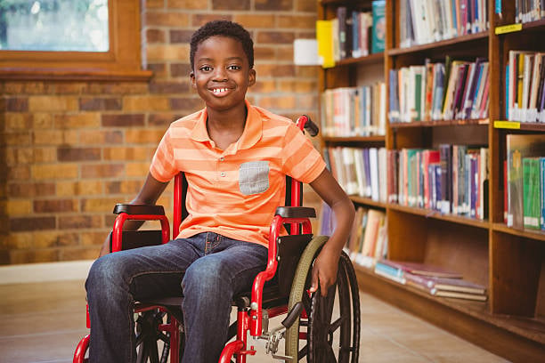 Menino sorrindo sentado em cadeira de rodas em uma biblioteca escolar