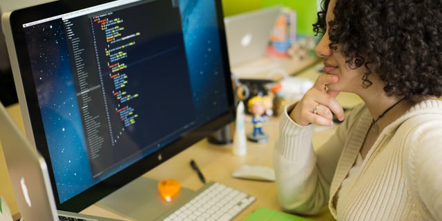Woman coding CSS with a code editor and large screen.