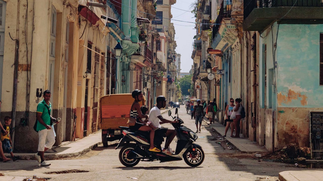 A narrow Havana street with a motorbike and pastel, weathered buildings, people going by, Cuba