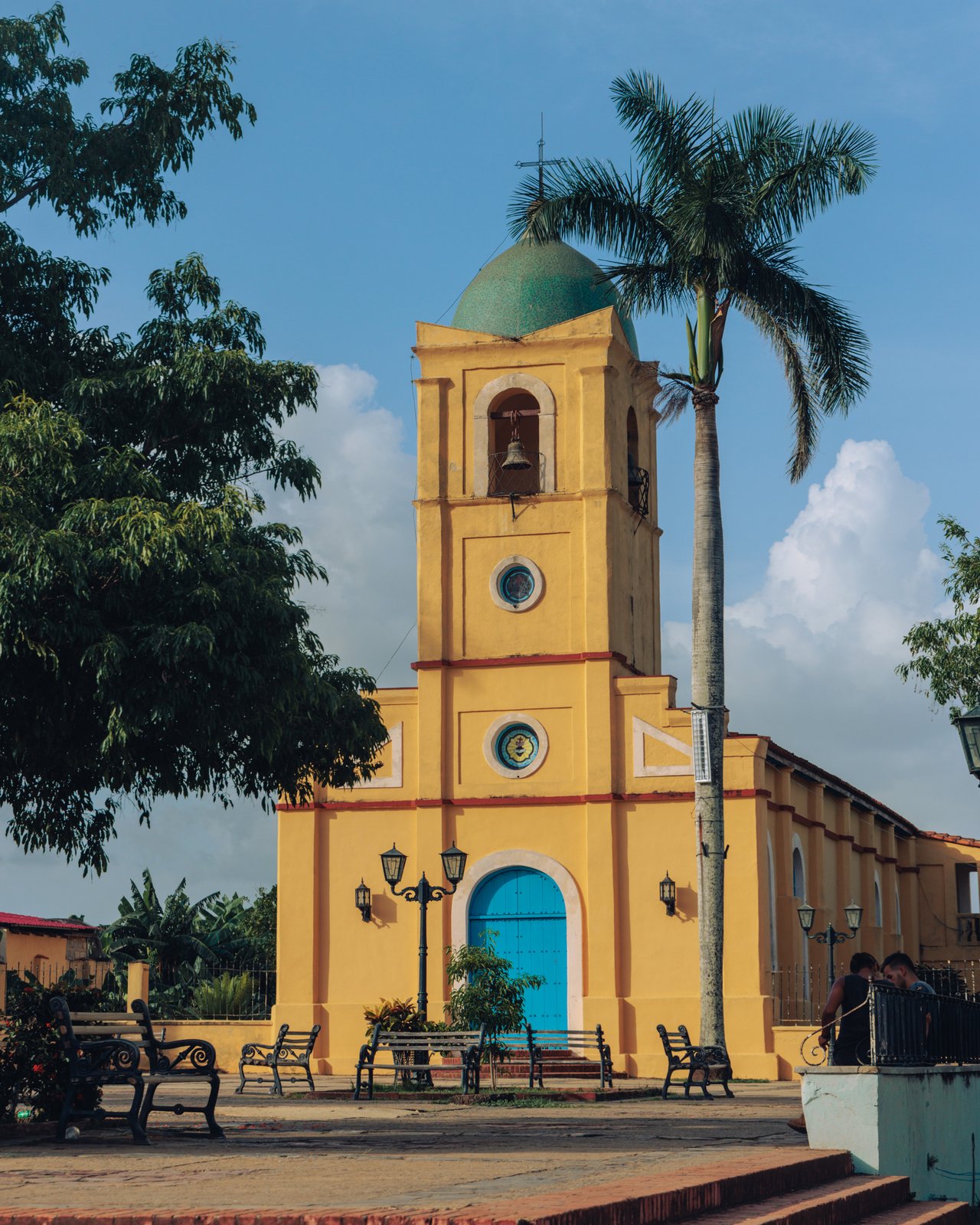 The yellow church of Viñales with its bell tower and dome beside a tall palm, Cuba