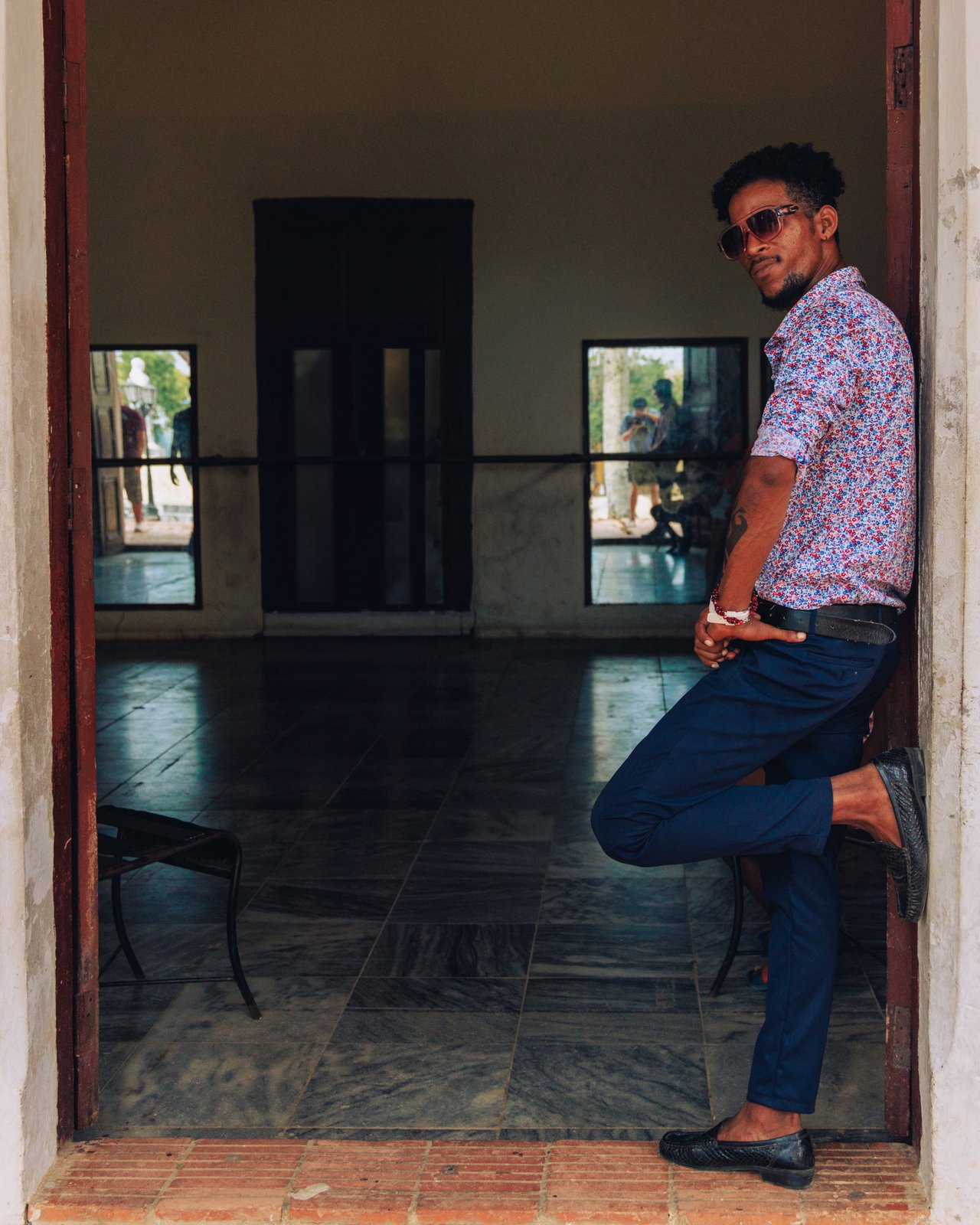 A young man in sunglasses leaning in the doorway of a colonial building, Cuba