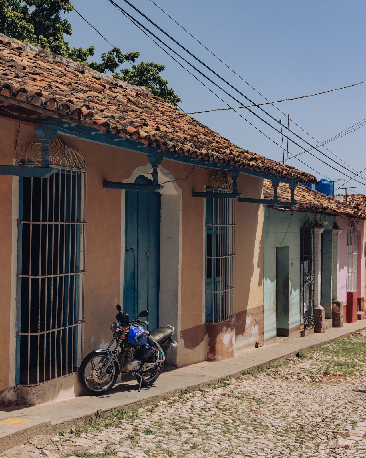 A cobbled Trinidad street of pastel colonial houses and tile roofs, a parked motorbike, Cuba