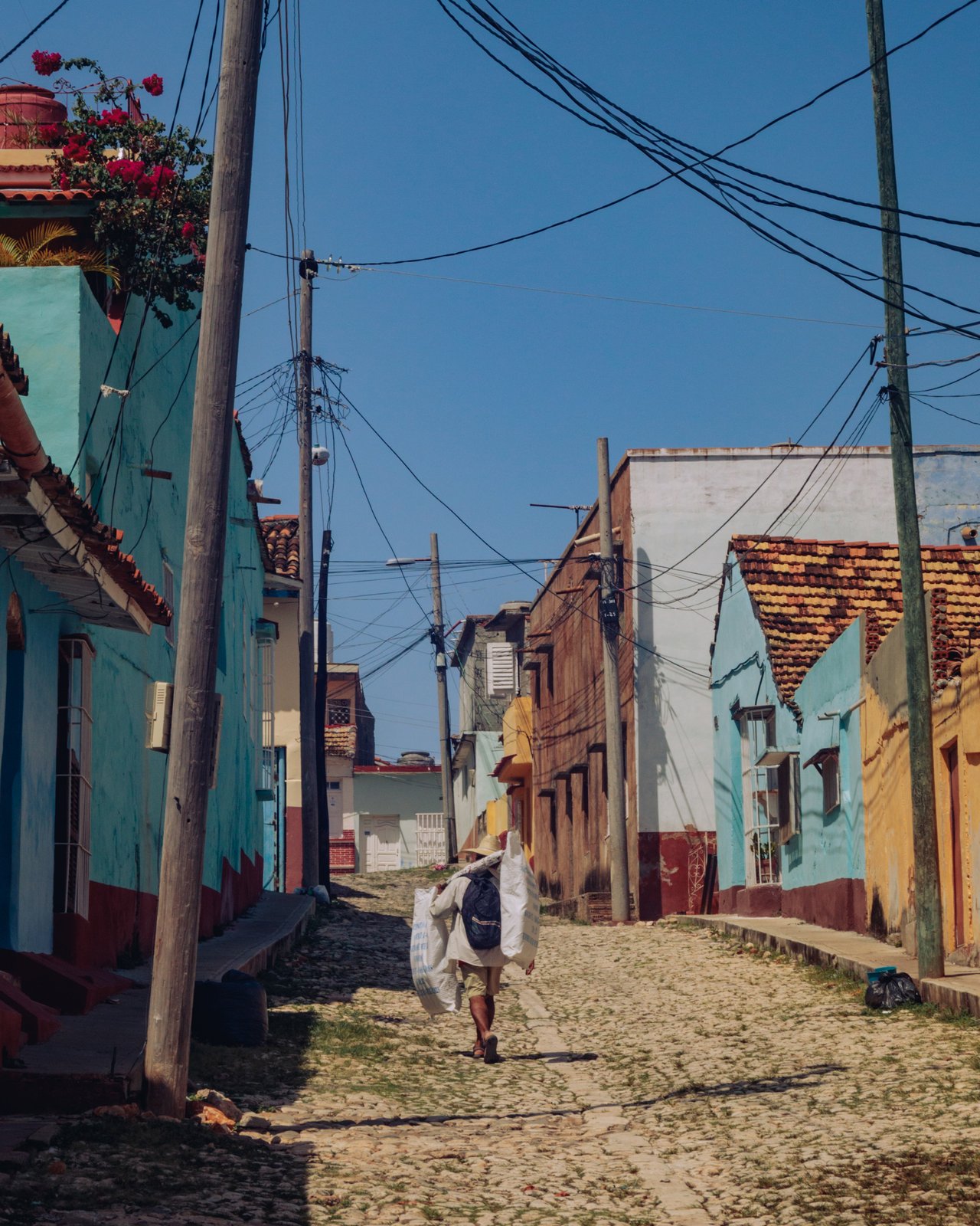 A man carrying a sack up a cobbled Trinidad street of tile-roofed houses, Cuba