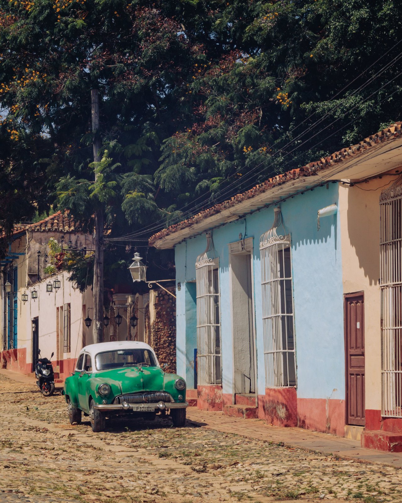 A green vintage American car parked on a cobbled street by a blue house, Trinidad, Cuba