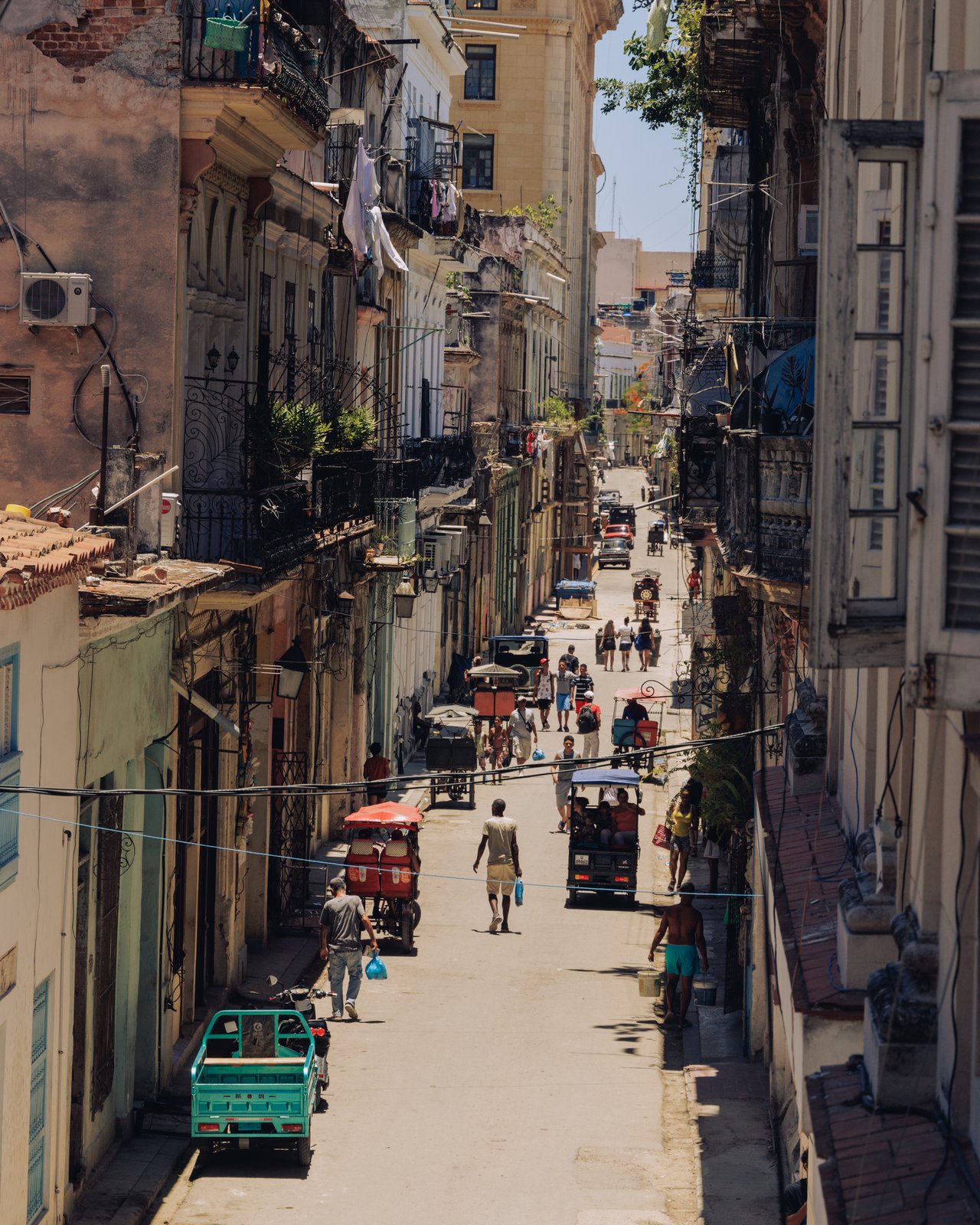 A steep Havana street from above — crumbling buildings, an auto-rickshaw and passers-by, Cuba