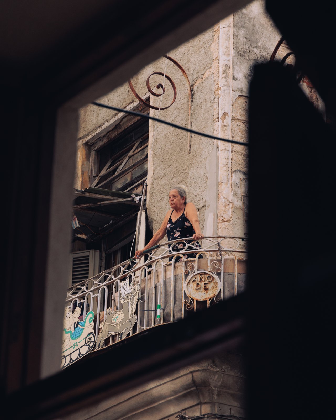 An older woman on a wrought-iron balcony of an old building, Havana, Cuba