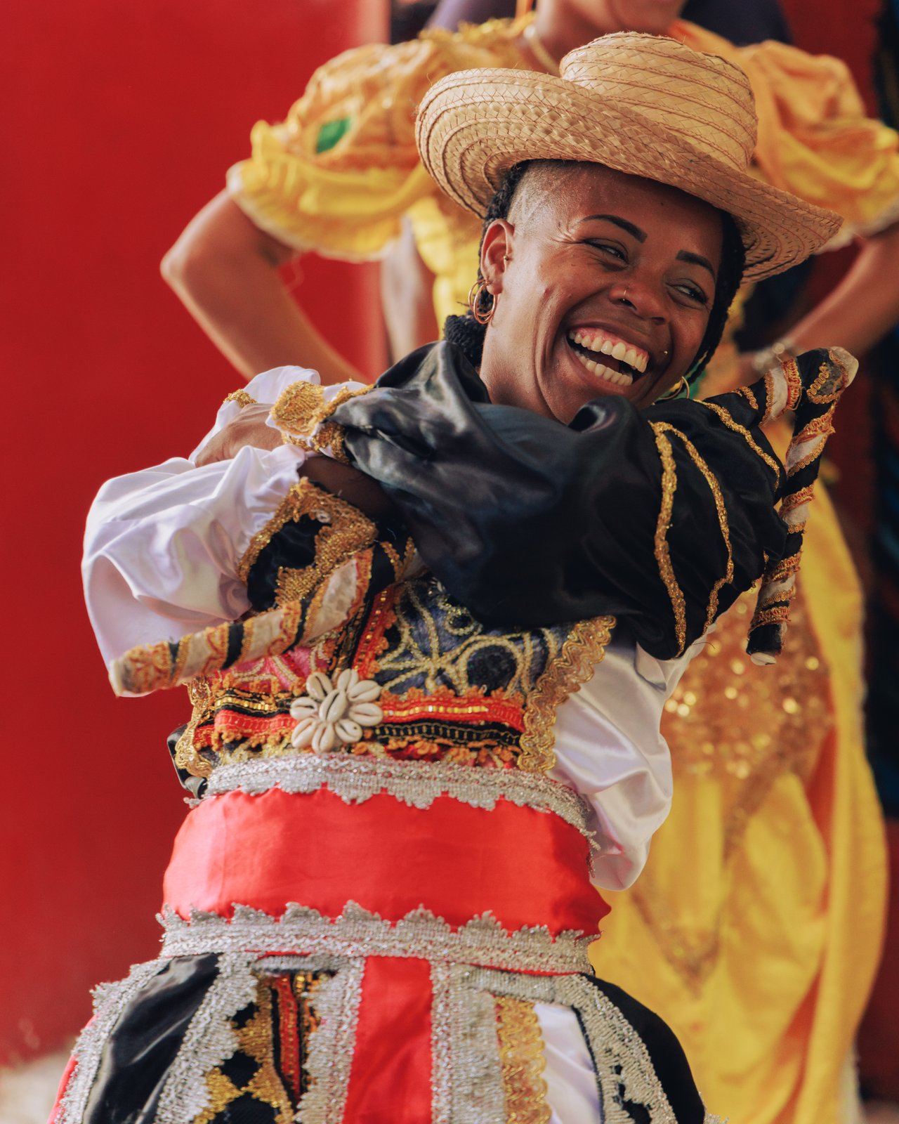 A laughing dancer in a yellow-and-red folkloric costume and straw hat, Cuba