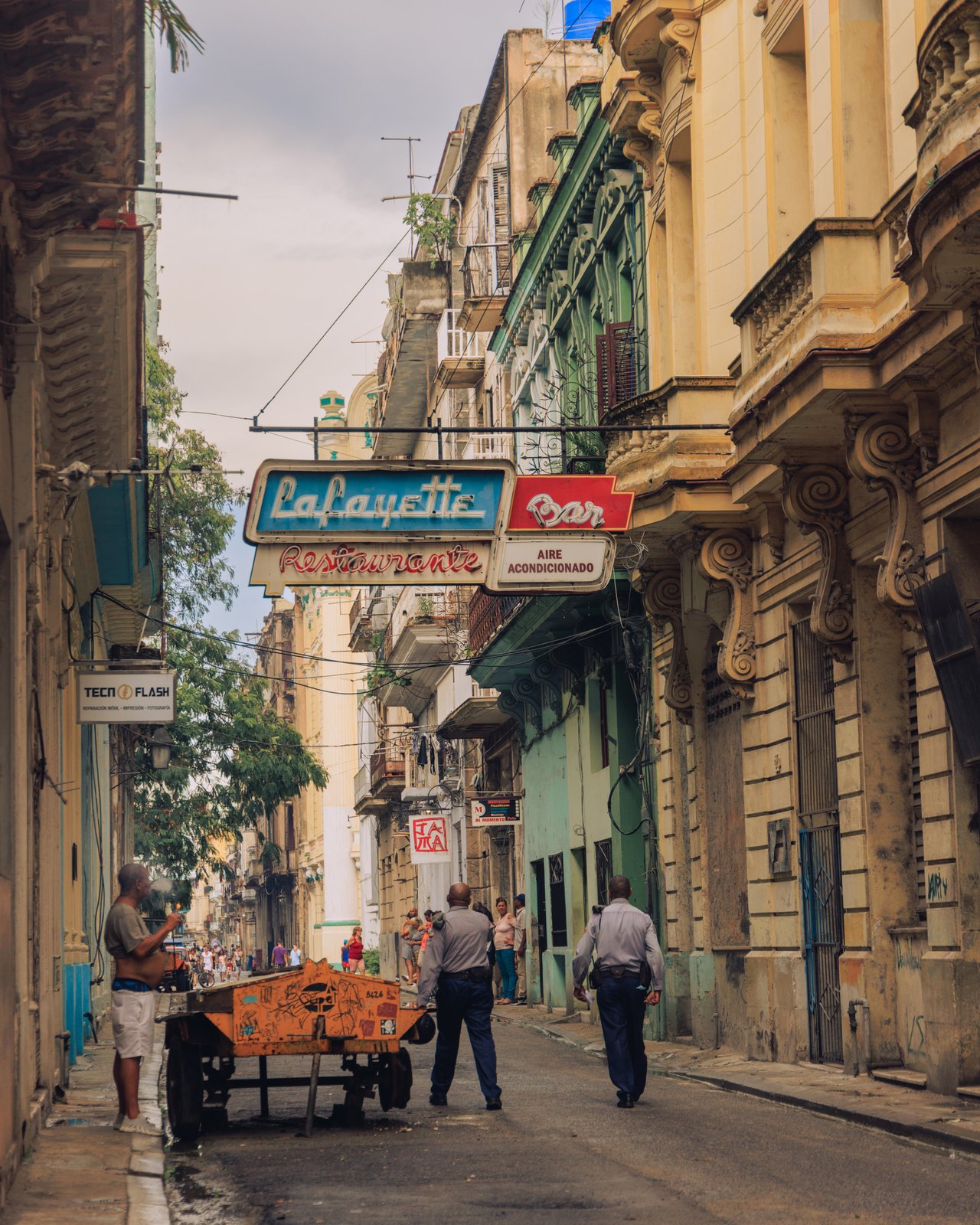 A Havana street under the 'Lafayette Bar' neon sign, men and an orange produce cart, Cuba
