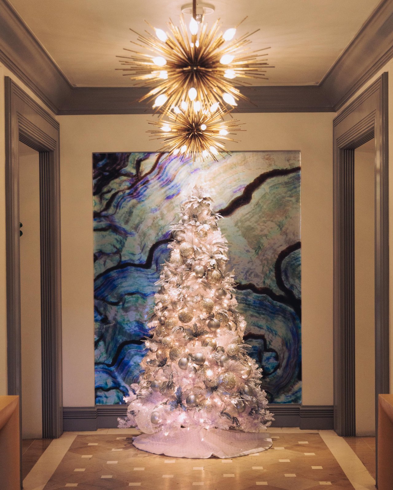 A flocked white Christmas tree before a large abstract artwork beneath a sputnik chandelier, Four Seasons Oʻahu