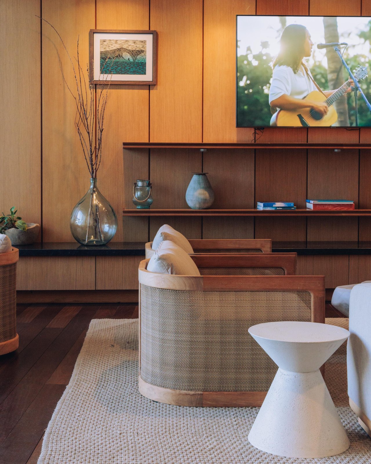A wood-panelled lounge with a woven armchair and styled shelves, Four Seasons Oʻahu