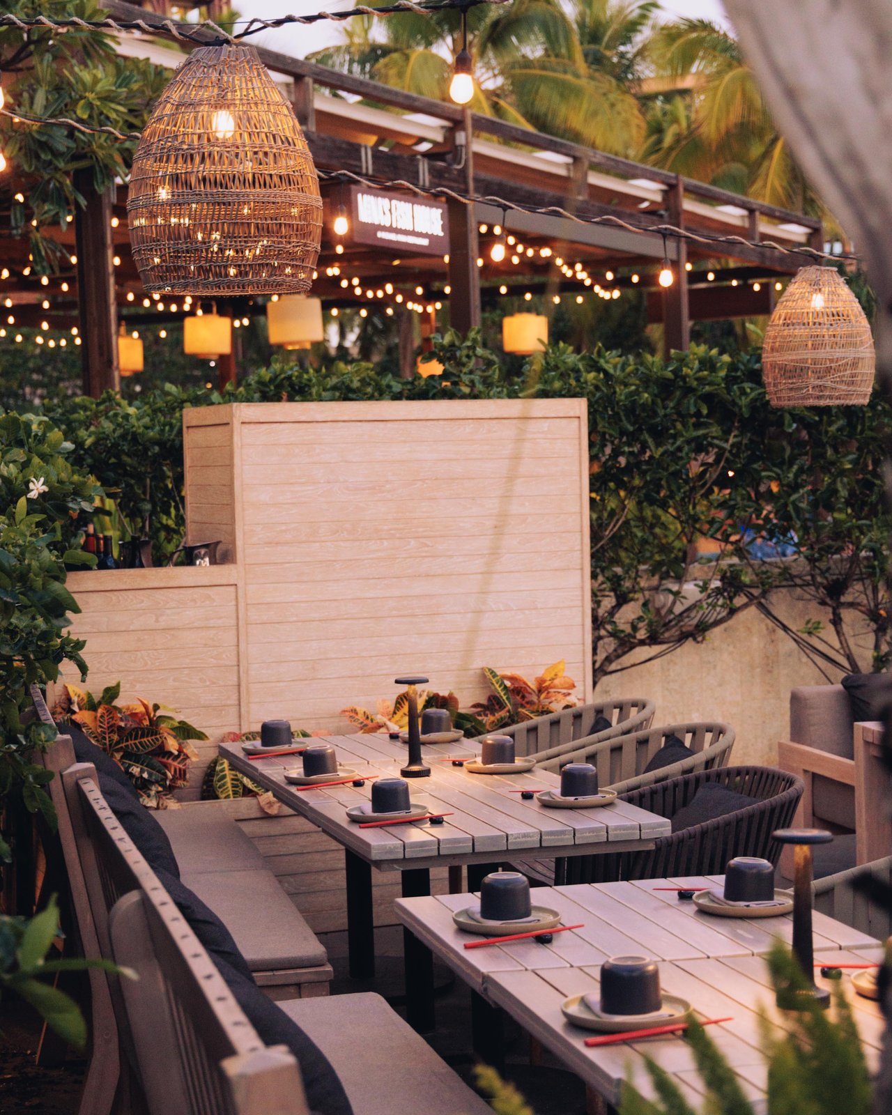 The terrace restaurant at dusk with woven pendant lights and low seating among palms, Four Seasons Oʻahu