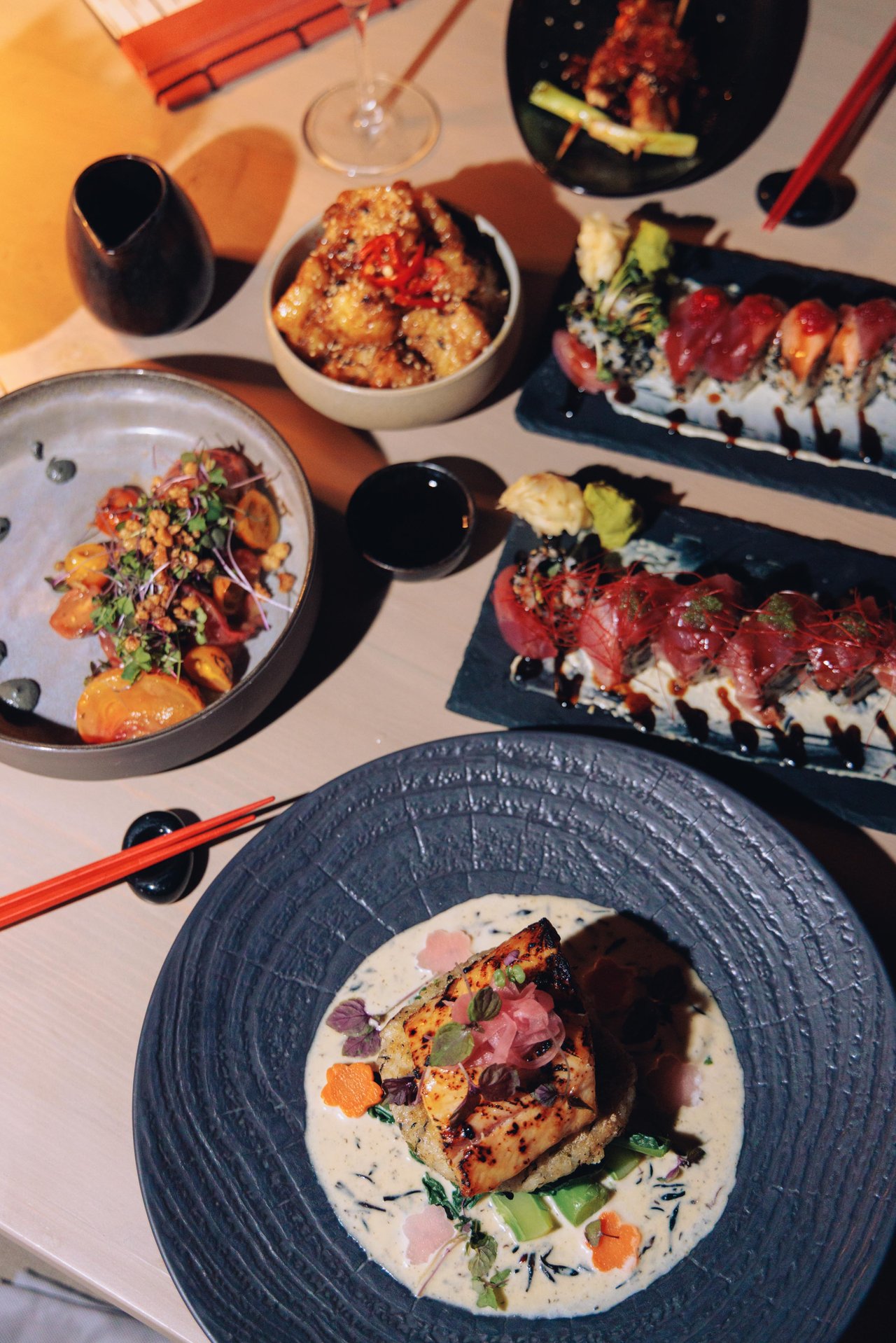 An overhead izakaya spread — sushi rolls, poke and a plated fish course, Four Seasons Oʻahu