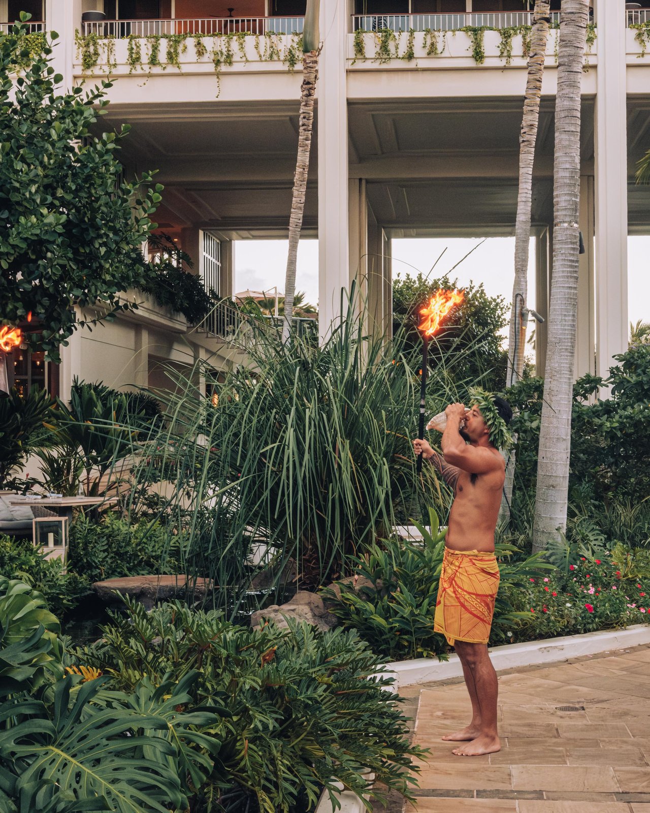 A Hawaiian performer in a sarong lighting a torch in the resort gardens, Four Seasons Oʻahu