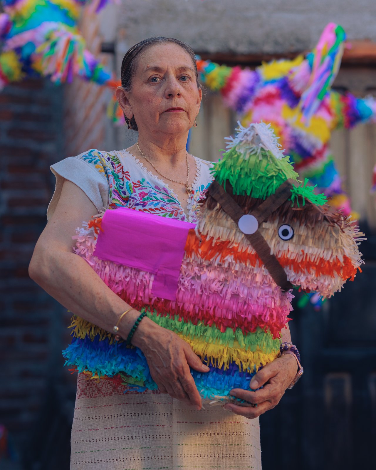 A woman in an embroidered blouse holding a handmade donkey piñata, Mexico