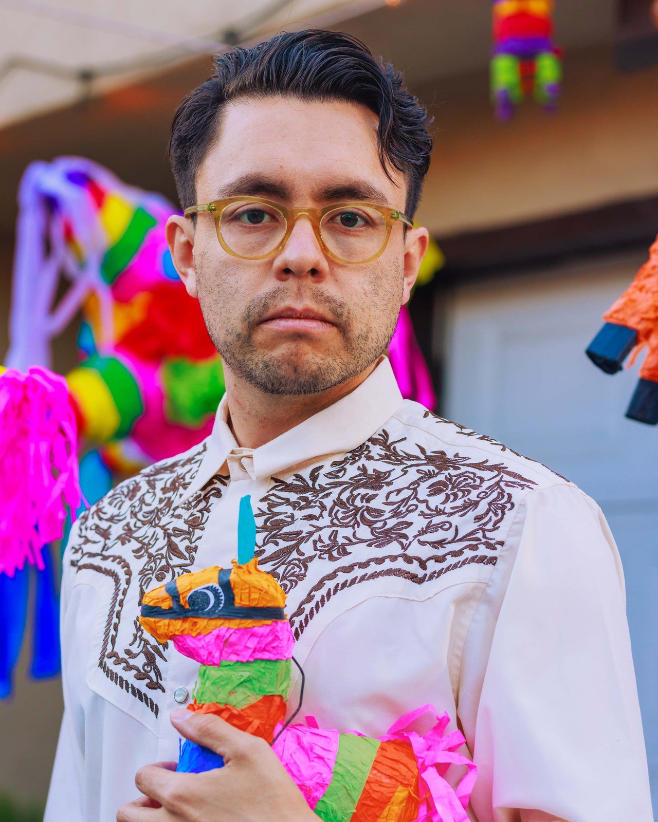 A man in an embroidered shirt and glasses cradling a small donkey piñata, Mexico