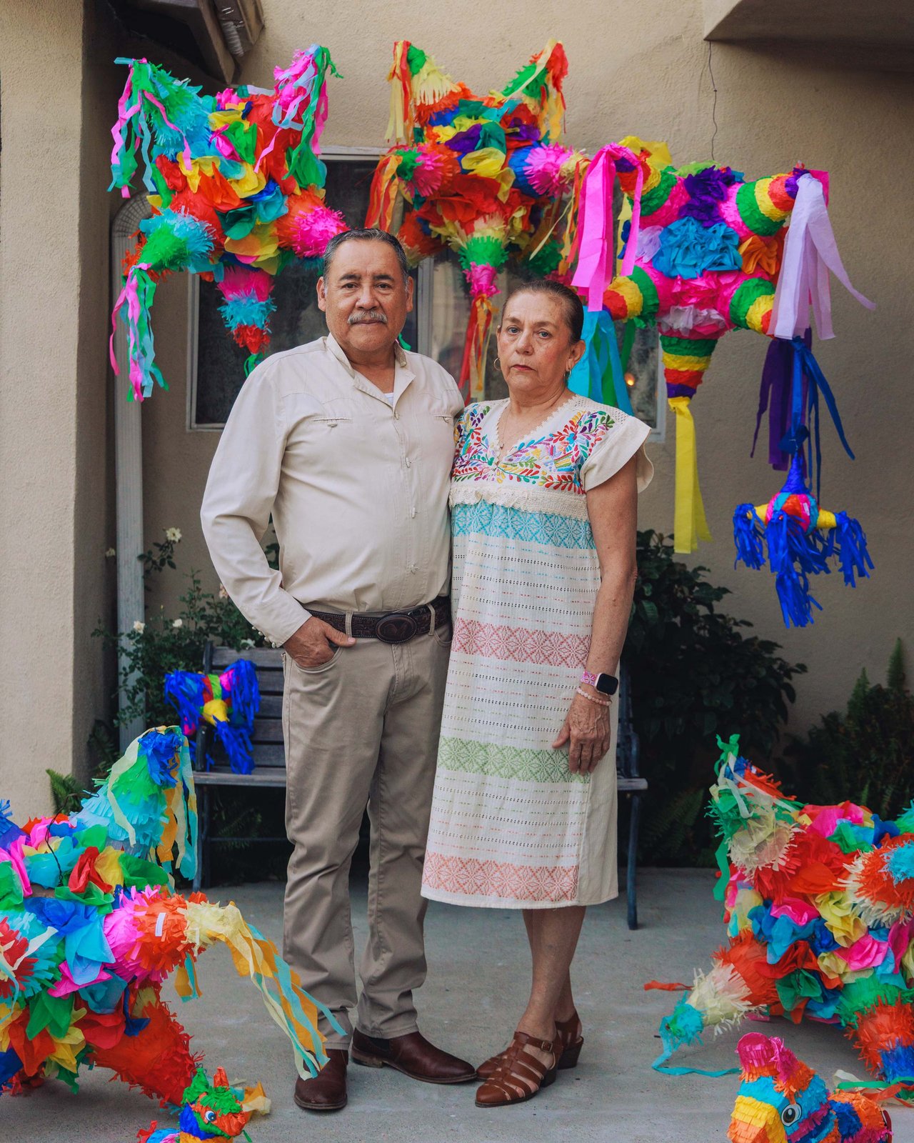 An older couple among the hanging piñatas of their courtyard, Mexico