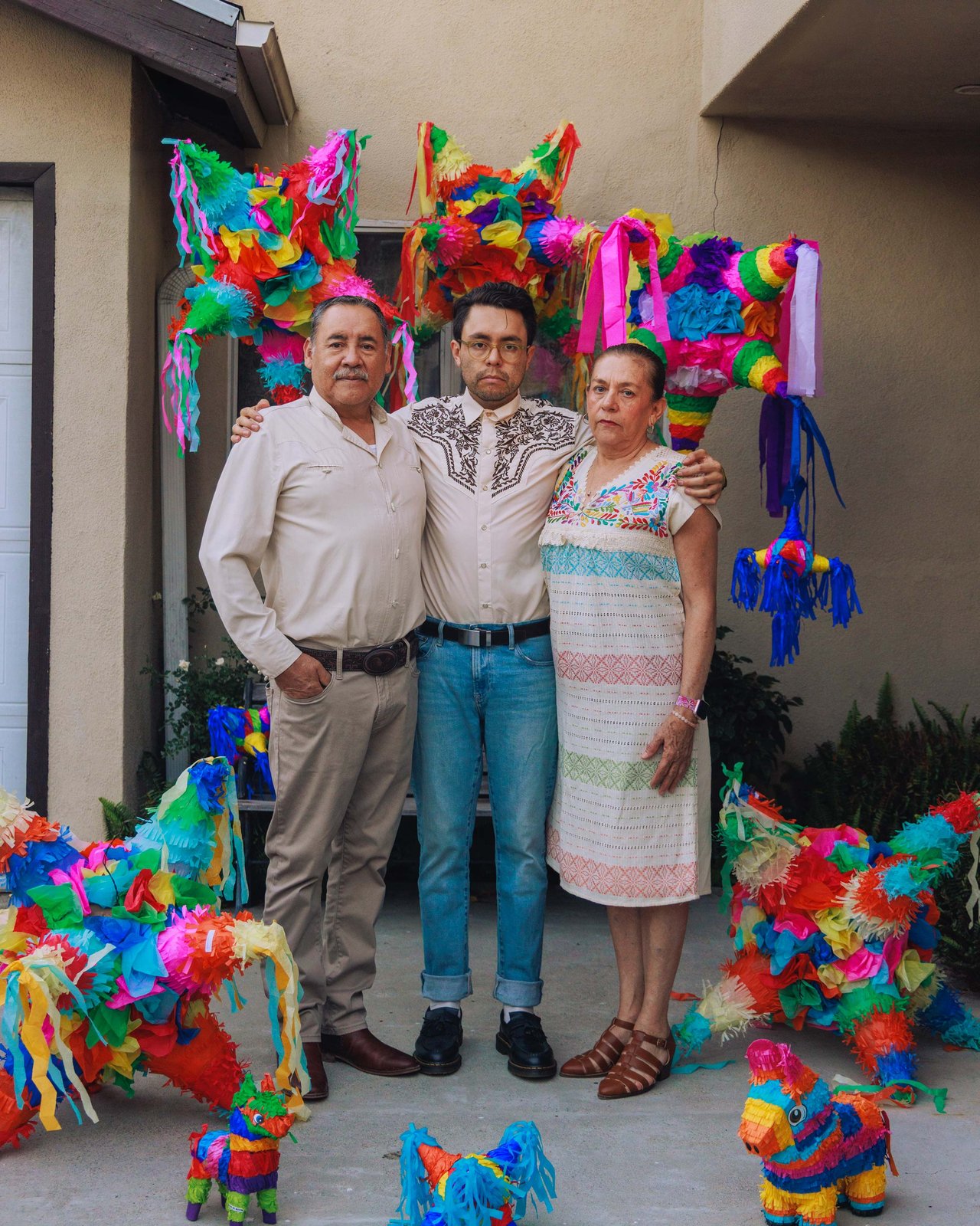 A family of three among the hanging piñatas of their courtyard, Mexico