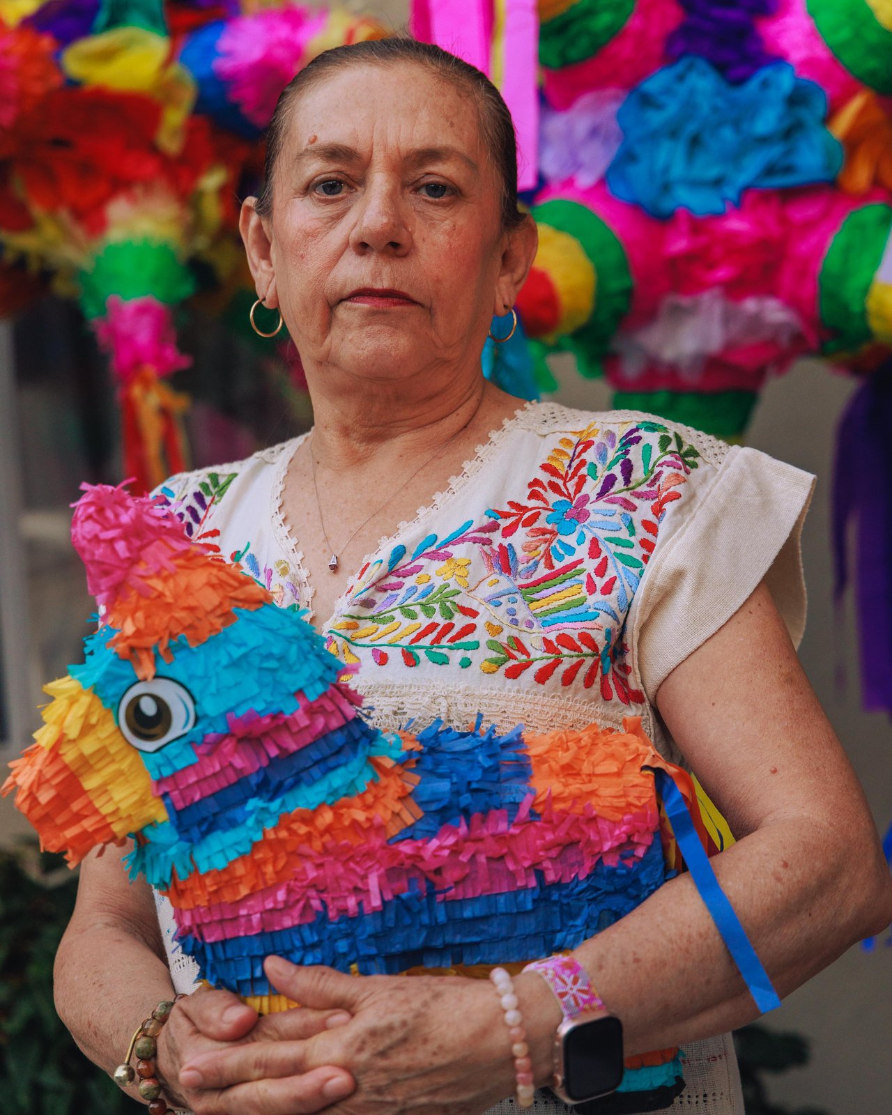 A woman in an embroidered blouse holding a rainbow piñata, Mexico