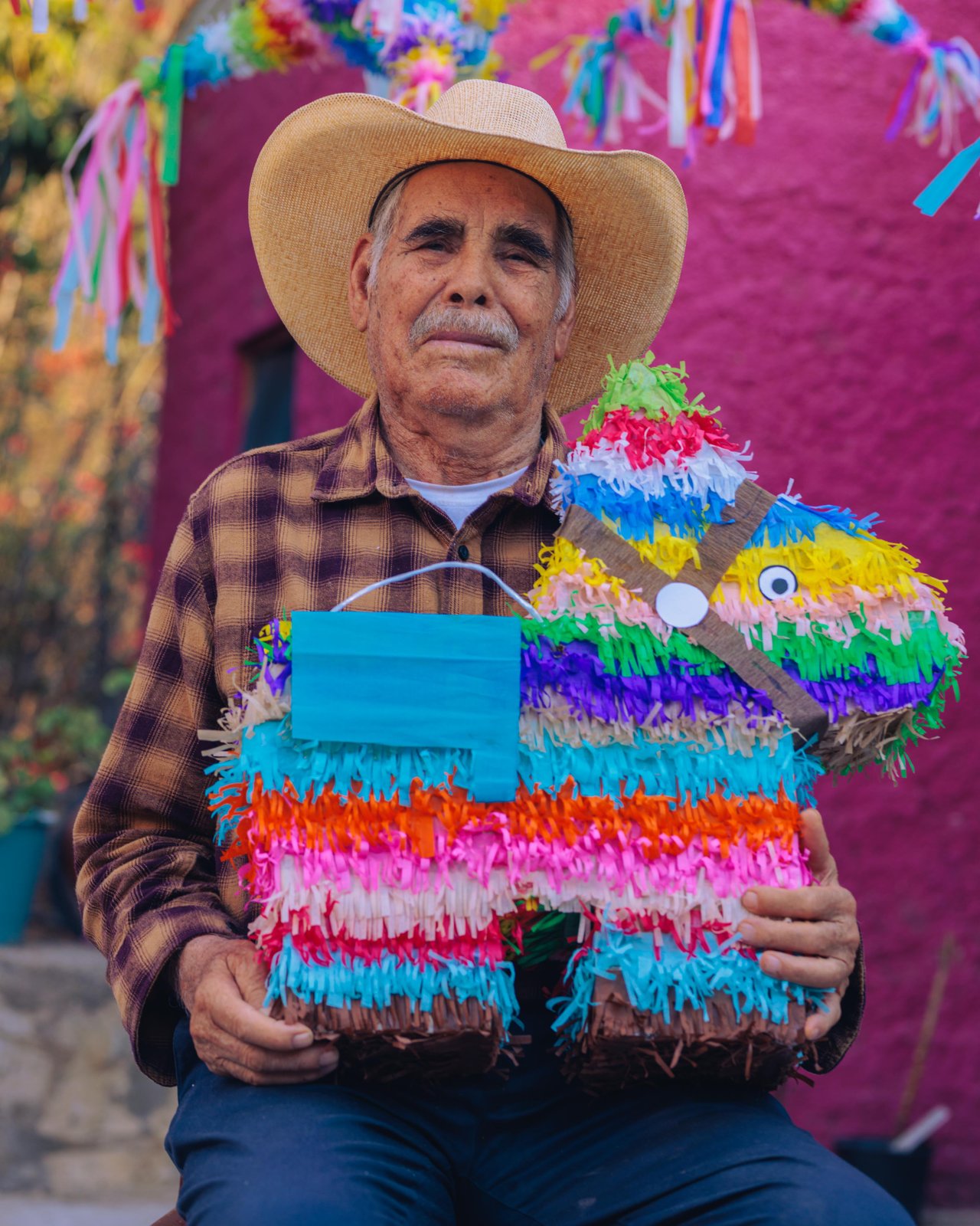A man in a straw hat holding a striped handmade piñata, Mexico